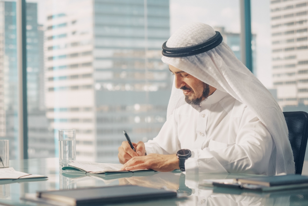 An Arab Person Drafting on a Paper in an Office.